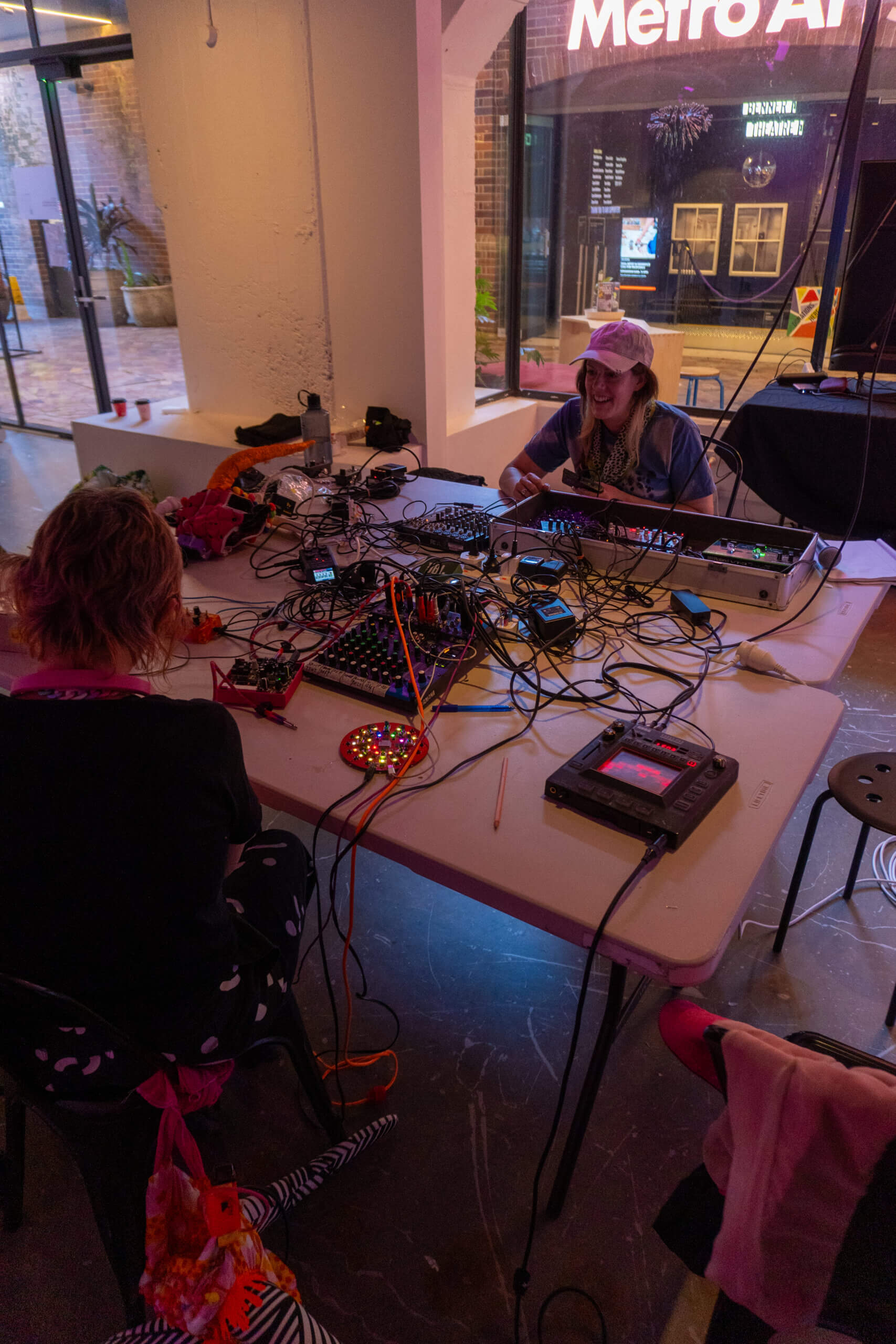 Alycia Bennett and Tara Pattenden at Metro Arts Gallery One, seated working together on synth electronics.